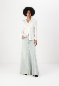 Camisa blanca de manga larga combinada con una falda maxi de mezclilla azul claro con un diseño acampanado y dobladillo deshilachado, llevada con zapatos negros.