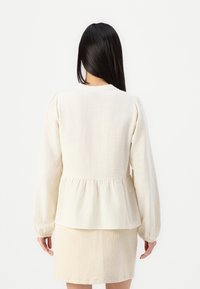 Harmaa vaaleanbeige pitkähihaisten paita, jossa on peplum-lantiot ja pehmeä rakenne, sekä hienovarainen rypytys olkapäillä, yhdistettynä yhdistelevään hameeseen.