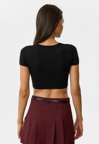 Zwarte crop top t-shirt met korte mouwen, aansluitend ontwerp, gladde textuur. Gecombineerd met een bordeauxrode plissérok en een zwarte riem.