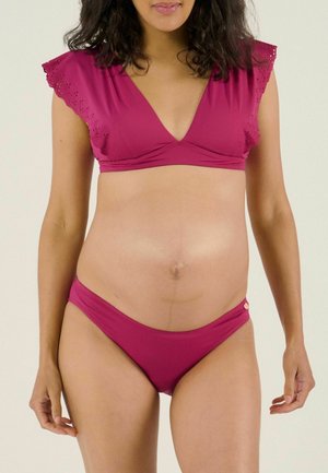 Frau trägt einen magentafarbenen Bikini mit Spitzenärmeln mit Lochmuster, zeigt ihren nackten Bauch und einen natürlichen Hautton.