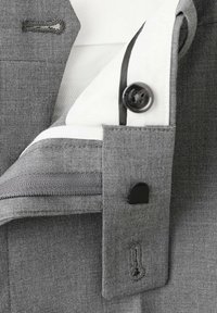 Gros plan d'un poignet de chemise gris avec un bouton noir, une boutonnière et une petite pince noire de fixation sur un tissu texturé.