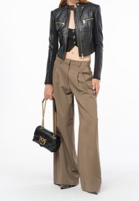 Zkrácená černá kožená bunda s kapsami na zip, spárovaná s béžovými kalhotami s vysokým pasem. Drží malou černou kabelku se zlatým řetízkem.