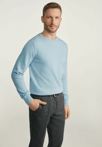 Jasnoniebieski sweter z okrągłym dekoltem, wykonany z miękkiego materiału, w zestawieniu z ciemnoszarymi, dopasowanymi spodniami. Sweter ma długie rękawy oraz prążkowane mankiety.