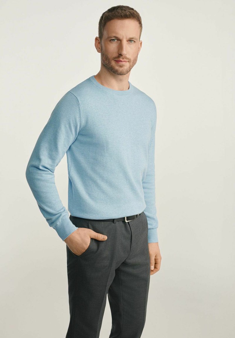 Jasnoniebieski sweter z okrągłym dekoltem, wykonany z miękkiego materiału, w zestawieniu z ciemnoszarymi, dopasowanymi spodniami. Sweter ma długie rękawy oraz prążkowane mankiety.