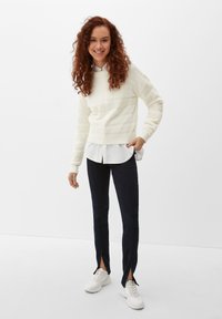 Romantisch gebreid sweater met gestructureerde strepen, gedragen over een wit overhemd met kraag, gecombineerd met marineblauwe broek met zijsplitten en witte sneakers.