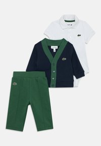 Tre-delad barnset: en vit polo-skorta, en marinblå cardigan med gröna accenter och gröna byxor. Material av bomull, med logodetaljer.
