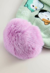 Vaaleanpunainen pörröinen pom-pom, joka on kiinnitetty vihreään sukkaan, jossa on sarjakuvamaisia pöllöjä. Pom-pomilla on pehmeä rakenne ja pyöreä muoto, jossa on purppuran sävy.
