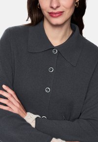 Grau gestrickter Cardigan mit Kragen, ausgestattet mit fünf Knöpfen, strukturiertem Stoff und cremefarbenen Spitzenmanschetten. Die Knöpfe sind rund und elegant.