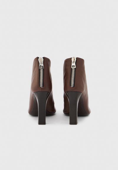 Bottes basses en cuir marron avec un talon bloc haut. Dotées d'une fermeture éclair arrière avec des accents métalliques et d'une texture lisse.