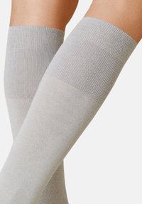 Graue knielange Socken aus einem glatten, gerippten Stoff, die eine einheitliche Struktur und eine einfarbige, minimalistische Gestaltung aufweisen.