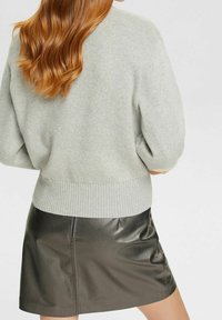 Jasnoszara, oversize'owa sweter z prążkowanym dołem i rękawami, w zestawieniu z czarną skórzaną spódnicą mini z zamkiem błyskawicznym z przodu.