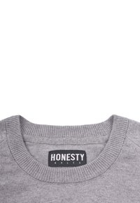 Grauer Sweatshirt mit geripptem Rundhalsausschnitt und einem Etikett mit der Aufschrift "EHRLICHKEIT REGIERT." Weiche Textur mit einfachem Design, ohne Muster oder Akzente.