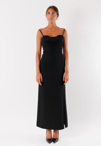 Abito midi nero aderente con scollatura a cuore, busto arricciato, spalline sottili e spacco laterale. Indossato con tacchi a punta neri.