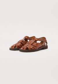Brune lærsandaler med flere stropper og spænde lukning. Har en flad sål og åben tådesign. Tekstureret overflade.