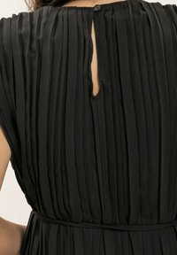 Robe plissée noire avec un col haut, une ouverture en forme de serrure à l'arrière et une ceinture en tissu à la taille, présentant une finition texturée.