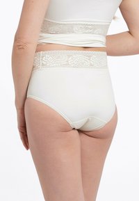 Mutande a vita alta color crema con cinturino in pizzo floreale e tessuto liscio ed elastico, progettate per comfort e supporto.
