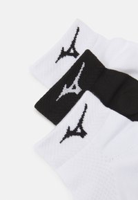 Tres pares de calcetines con un diseño tejido texturizado en blanco y negro, con un logotipo negro prominente y puños acanalados en contraste.