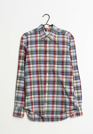 Chemise à manches longues avec boutons, à motif écossais rouge, bleu, vert et blanc, suspendue à un cintre noir sur fond blanc.