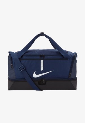 Mørkeblå treningsbag med svart bunn, justerbar skulderrem, doble glidelåser og fremtredende hvit Nike swoosh-logo på fronten.