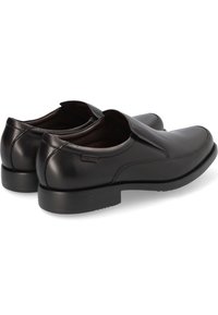 Zapatos negros de cuero sin cordones con un acabado suave, punta redondeada, tacón bajo y paneles laterales elásticos para facilitar su uso. Detalle sutil del logo visible.