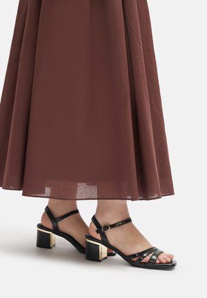 Sandalias de tacón negras con tiras, con punta cuadrada, tacón cuadrado con acento dorado y correa ajustable en el tobillo.