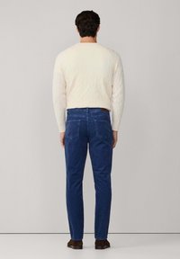 Pantalones de pana azul con dos bolsillos traseros, combinados con un suéter de punto trenzado crema y zapatos marrones, vistos desde la parte posterior.