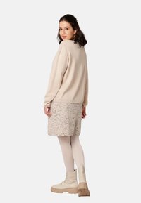 Hellbeiger Pullover mit langen Ärmeln, kombiniert mit einem strukturierten Rock mit bunten Sprenkeln. Gestylt mit beigen Ankle Boots.