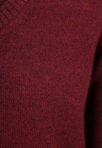 Karmesinroter gestrickter Pullover mit V-Ausschnitt, aus einem weichen, strukturierten Stoff gefertigt, der ein leicht meliertes Aussehen aufweist.