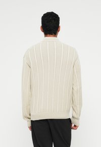 Suéter de lã em tom creme, com listras verticais grossas, apresentando um gola e punhos canelados. Ajuste solto com tecido texturizado.