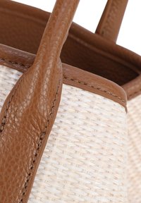 Una borsa a tracolla intrecciata con un corpo di colore crema testurizzato, manici e rifiniture in pelle marrone, che evidenzia il contrasto tra i materiali.