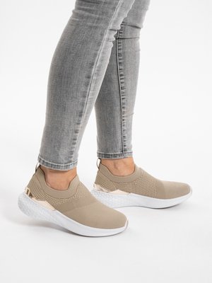 Person wearing beige knit slip-on sneakers with white soles and metallic accents, paired with fitted light gray jeans.