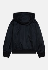 Chaqueta negra con capucha que presenta una textura suave y brillante, puños y cintura elásticos, con un corte relajado y un detalle minimalista.