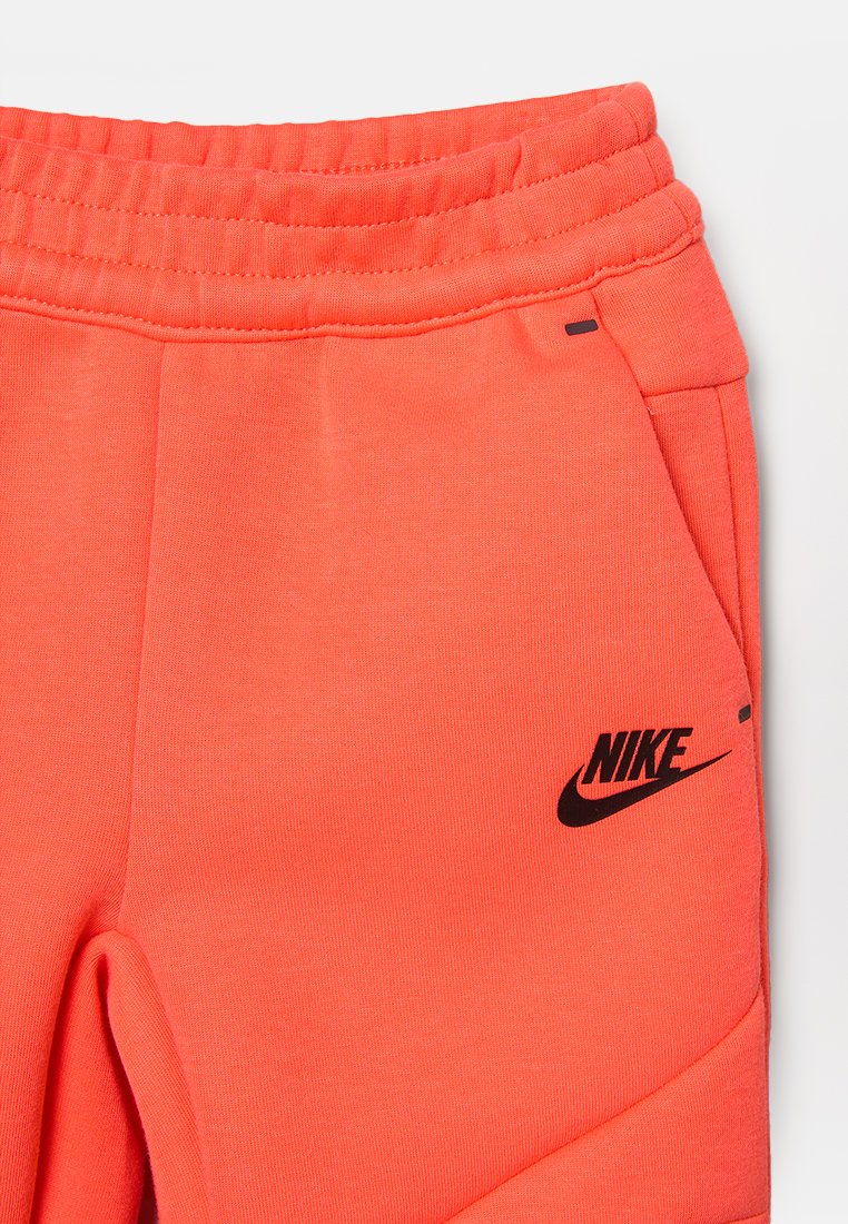 Korallowe dresowe spodnie Nike z elastycznym pasem, bocznymi kieszeniami i czarnymi akcentami logo. Materiał wydaje się miękki i ma gładką teksturę.