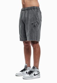 Pilki medvilniniai šortai su elastiniu juosmeniu, šoninėmis kišenėmis ir išsiuvinėta logotipo detale. Derinami su pilkais ir baltais aukštakulniais sportbačiais.