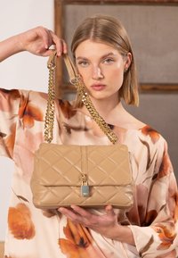Beige gesteppte Handtasche mit goldener Kette und Lederhenkel. Verfügt über eine Klappe mit metallischem Akzent. Glatte Oberfläche, rechteckige Form.