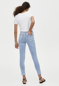 Jeans ajustados de color azul claro, confeccionados en denim, con cintura alta, bolsillos traseros y una silueta ceñida. Combinados con una camiseta blanca básica.