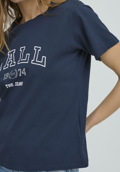 Tricou din bumbac bleu marin cu mâneci scurte, având text alb, "1984 EST. JEANS," și un guler rotund simplu.