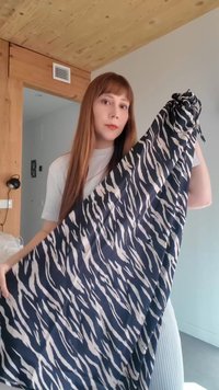 Γυναίκα με μακριά καστανά μαλλιά κρατάει ένα ύφασμα μαύρο-άσπρο με ρίγες ζέβρας σε ένα δωμάτιο με ξύλινη οροφή και ανοιχτό γκρι τοίχους.