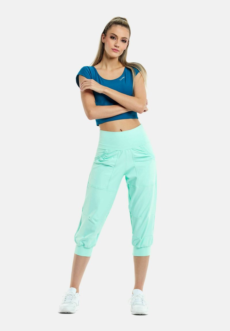 Tyrkysový crop top a mätovo zelené capri nohavice. Nohavice majú dve predné vrecká a elastické manžety, sú vyrobené z mäkkého, elastického materiálu.