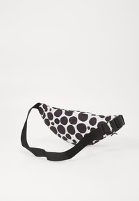 Fanny pack su baltu audiniu, padengtu dideliais juodais taškeliais, kreivos formos ir reguliuojama juoda dirželiu su plastikiniu sagtimi.