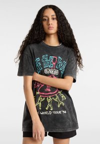 Camiseta negra gráfica con el texto colorido "OFF THE WALL" y un diseño de guitarra, con un corte relajado y textura desgastada.