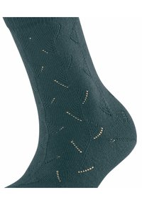 Zielona dzianinowa skarpetka z teksturowanym wzorem i jasnymi złotymi akcentami. Wzór zawiera niewielkie geometryczne motywy na całej powierzchni.