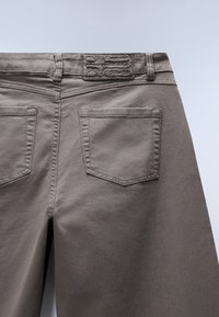 Graue Denim-Hosen mit glatter Textur. Mit zwei Gesäßtaschen und einem strukturierten Taillenlabel. Einfaches, utilitaristisches Design.