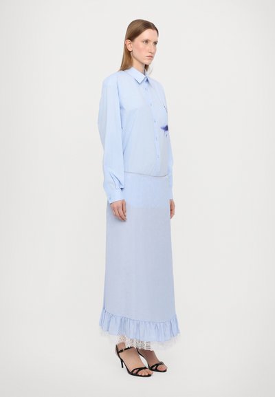 Abito lungo di colore azzurro chiaro con una parte superiore a camicia con bottoni e orlo a balze. Realizzato in tessuto morbido, presenta una leggera trama e un dettaglio in pizzo.