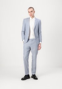 Costum bleumarin deschis, croit din țesătură, format dintr-o jachetă cu un singur nasture, rever cu vârf, pantaloni slim și pantofi negri eleganți.