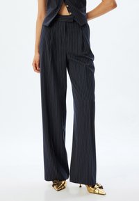 Pantalons larges à rayures marines, dotés d'une texture lisse et d'une taille haute avec une coupe ajustée. Les détails en métal incluent des boutons dorés.