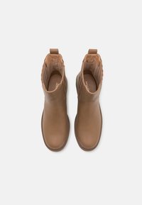 Para brązowych skórzanych botków za kostkę z zaokrąglonymi noskami i pętelkami do wkładania, widocznych z góry na białym tle.