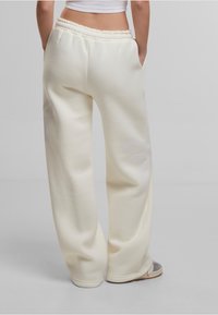 Pantalons de survêtement crème à coupe ample avec une taille élastique à cordon de serrage, poches latérales et accents de design ton sur ton subtil sur les jambes. Texture de tissu douce.