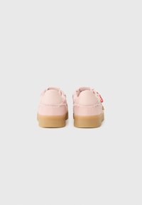 Pink athletic shoes with a smooth upper, frayed edges, and a gum sole. Features a small red tag on one side for added detail.