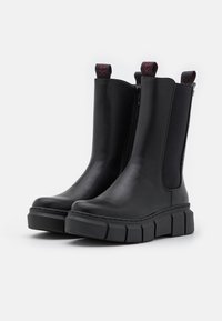 Botas de cuero negras hasta el tobillo con paneles elásticos en los laterales y cierre de cremallera, que cuentan con una suela de goma negra gruesa y texturizada y tiradores.